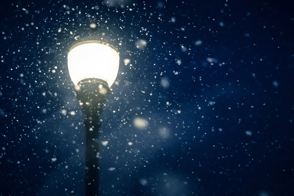 Heavy snow flowing around bright street lamp after dark