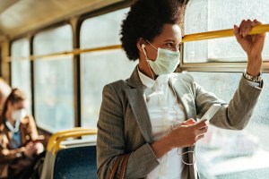 woman wearing mask on bus holding smartphone