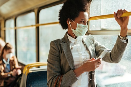 woman wearing mask on bus holding smartphone