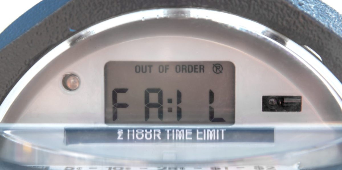 Closeup of the top of a parking meter that says FAIL. Meter also says OUT OF ORDER. Focus on words but dirt on glass makes text appear less sharp.
