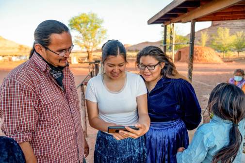 Photograph of a Navajo Family looking down and smiling at a smart phone