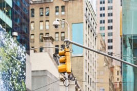 Security camera and traffic light are mounted on a pole, keeping watch over a bustling city street in New York City.