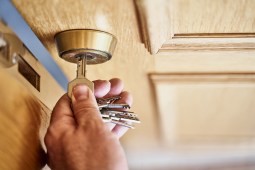 above view of caucasian person arriving close home holding a key opening a wooden door and taking out the key from the lock. The locksmith is old and rusty.