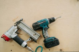 Well-used cordless drill and pneumatic nail gun lying on a plywood surface, ready for the next construction or diy project