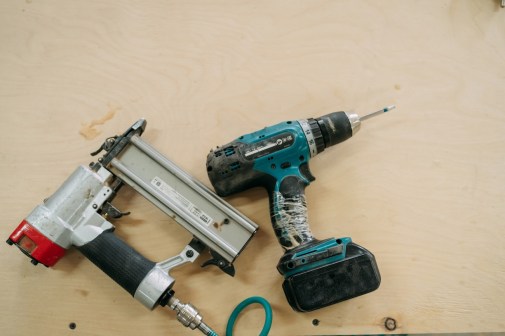 Well-used cordless drill and pneumatic nail gun lying on a plywood surface, ready for the next construction or diy project