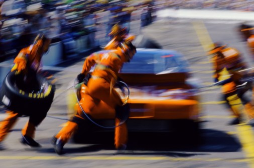 A blurry image of an auto racing pit crew servicing a race car mid-race.