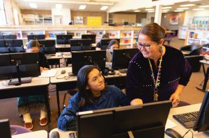 A Navajo male student works on an assignment in the library computer lab with the help from a teacher. Image taken on the Navajo Reservation, Utah, USA.