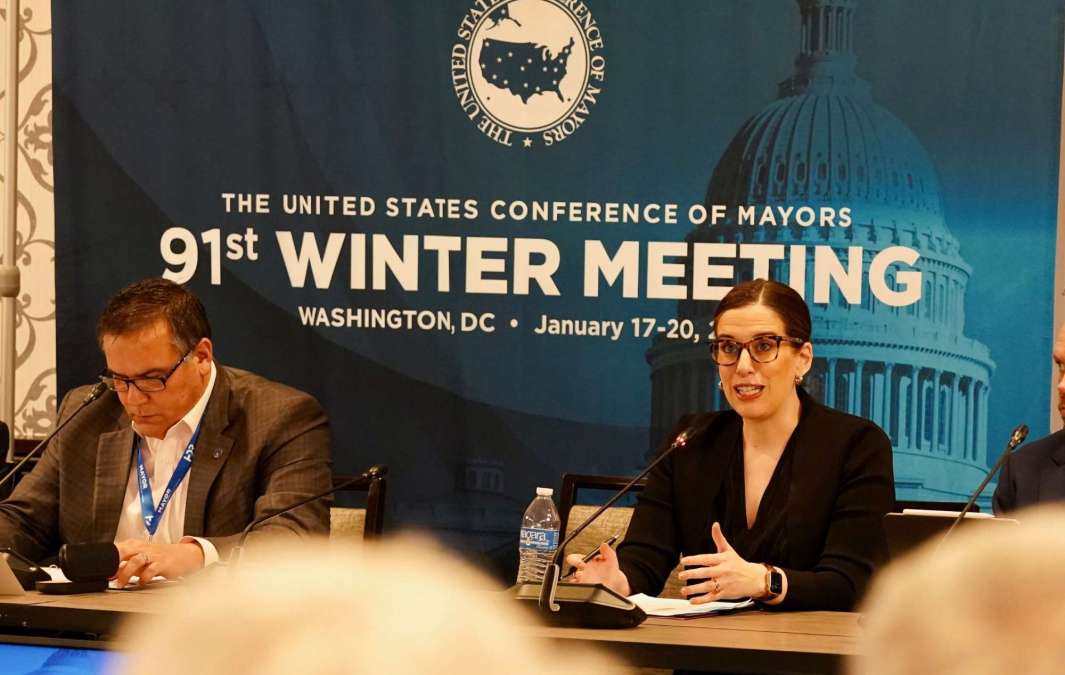 Photograph of a conference meeting showing Sarah Morris addressing the US Conference of Mayors